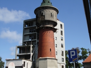 Stara wieża ciśnień wody i doń przyklejony nowy budynek.